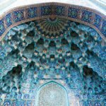 A close-up view of an ornate Islamic dome with vibrant blue mosaic patterns and geometric design.